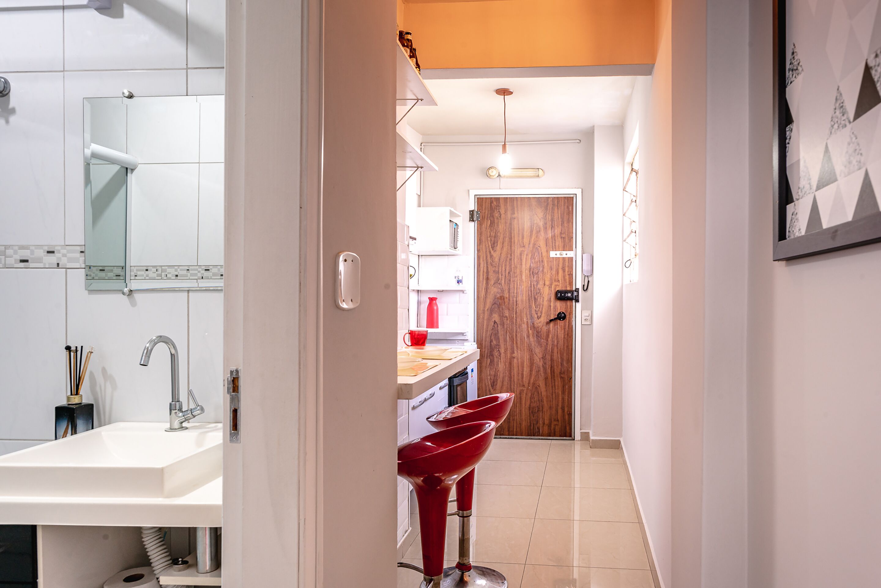 Una cocina moderna con un lavamanos blanco, taburetes rojos y una puerta de madera.