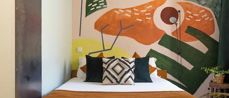A bed with a brown blanket, a geometric patterned pillow, and a wall with abstract art.