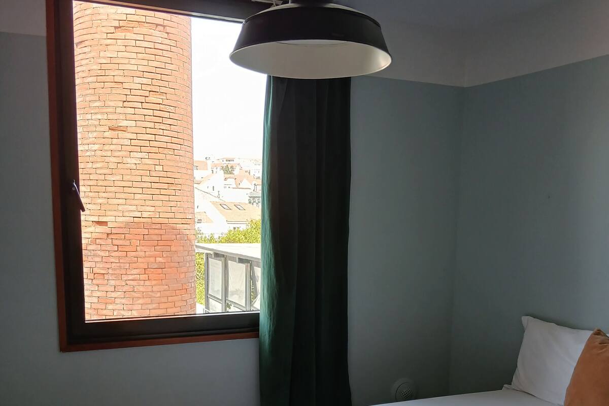Ein Schlafzimmer mit Bett, einem Fenster mit Vorhängen und einer Pendelleuchte.