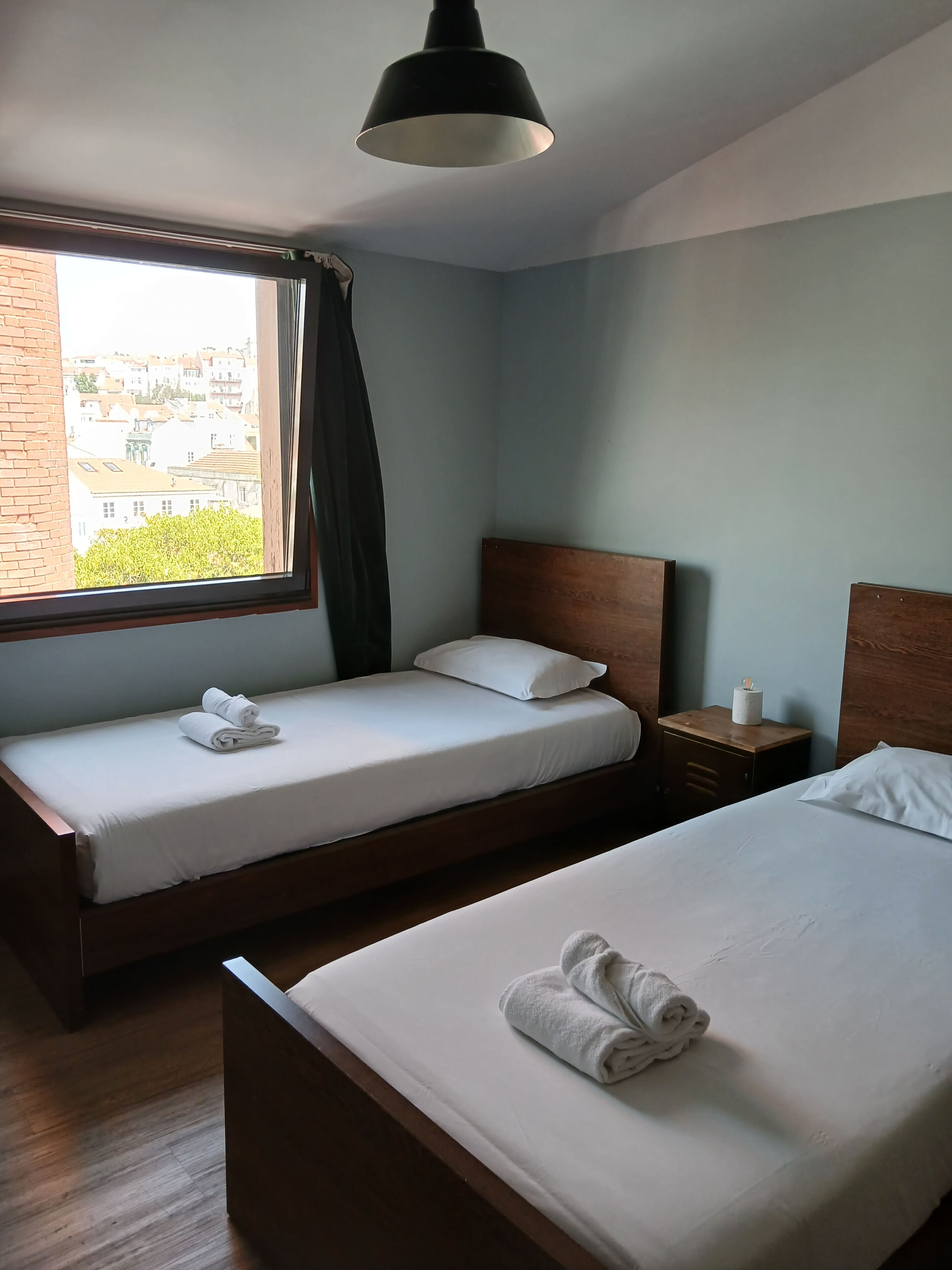 Een hotelkamer met twee bedden, een raam met gordijnen, een houten hoofdeinde, een nachtkastje en een lamp.