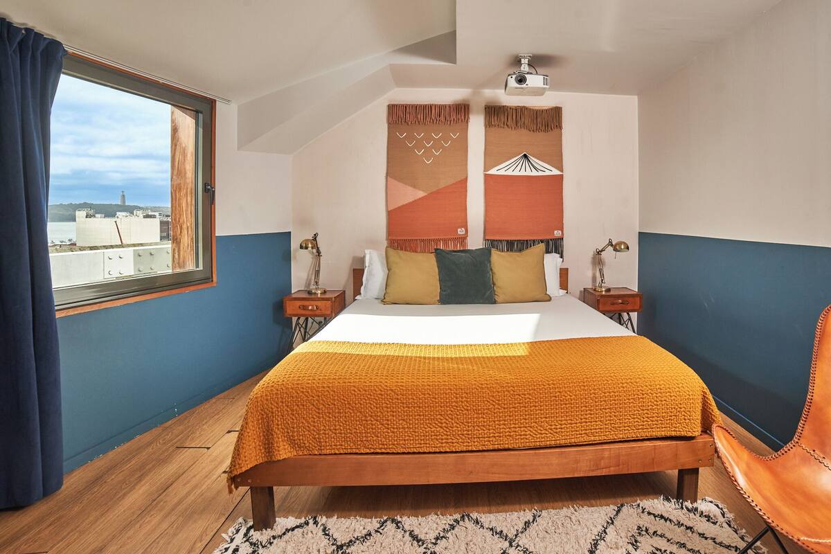 Ein Schlafzimmer mit einem Bett, zwei Nachttischen, einem Fenster und Blick auf die Stadt.