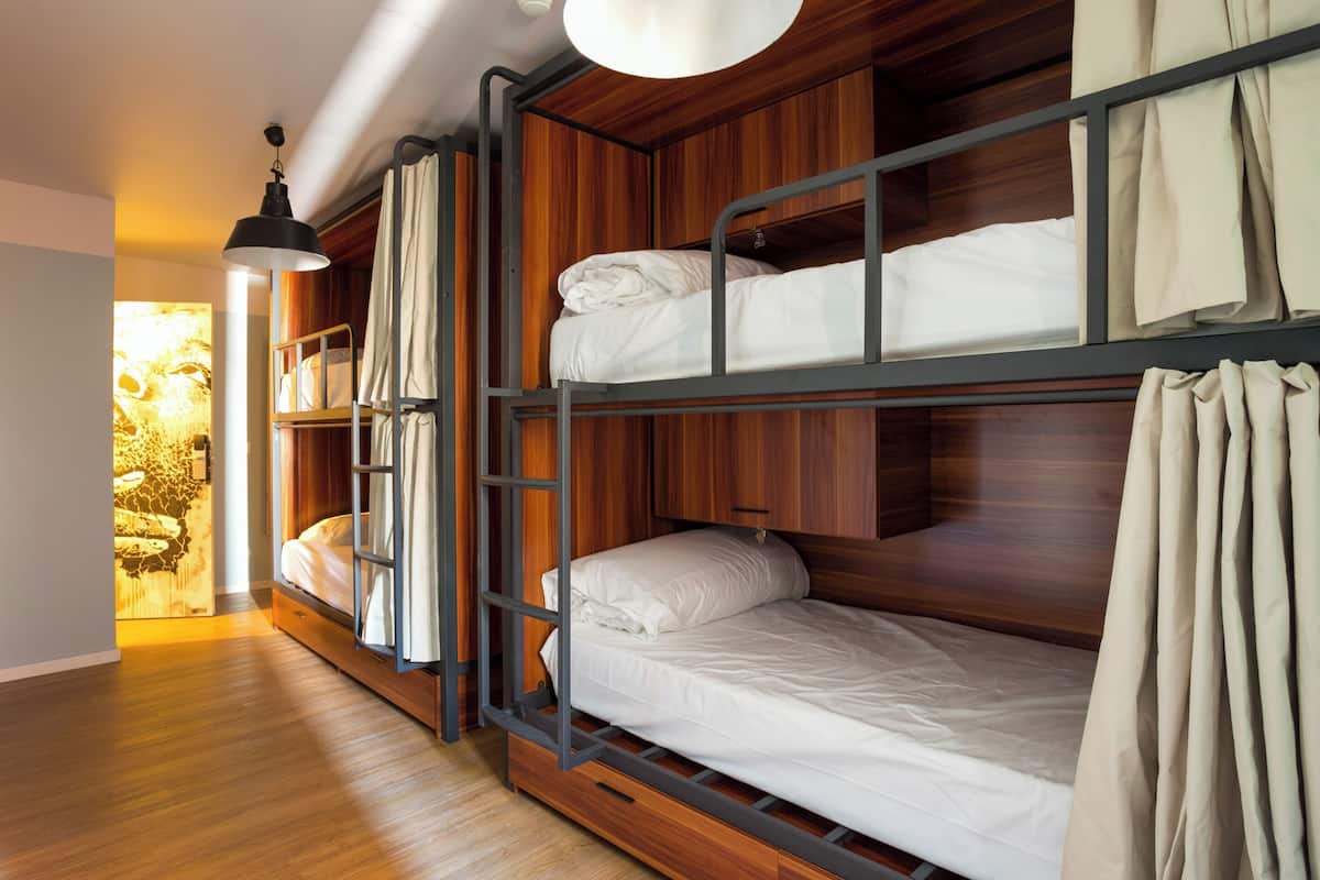 Habitación con literas, paneles de madera, lámpara colgante y ventana con cortinas.