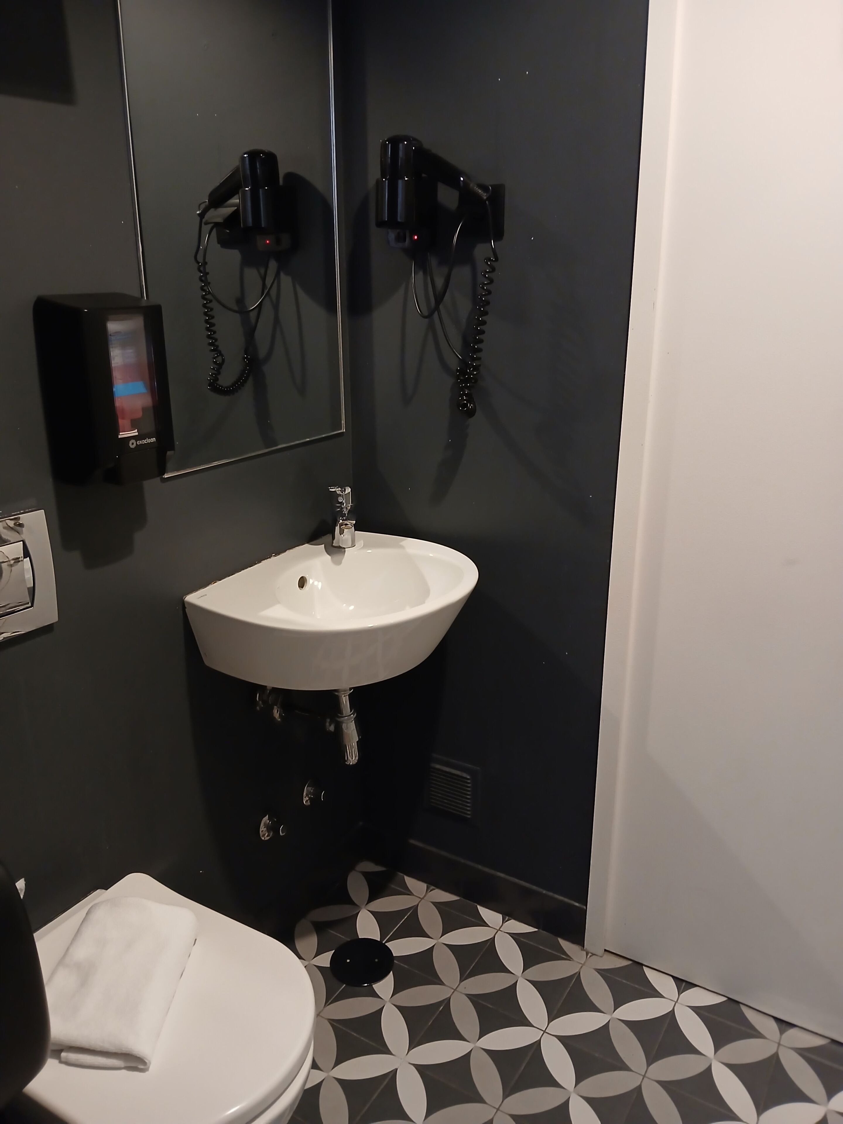 A bathroom with a white sink, a mirror, a hairdryer, and a towel on the toilet.
