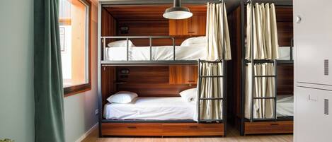 A bunk bed room with wooden walls, a ceiling fan, and a window with curtains.