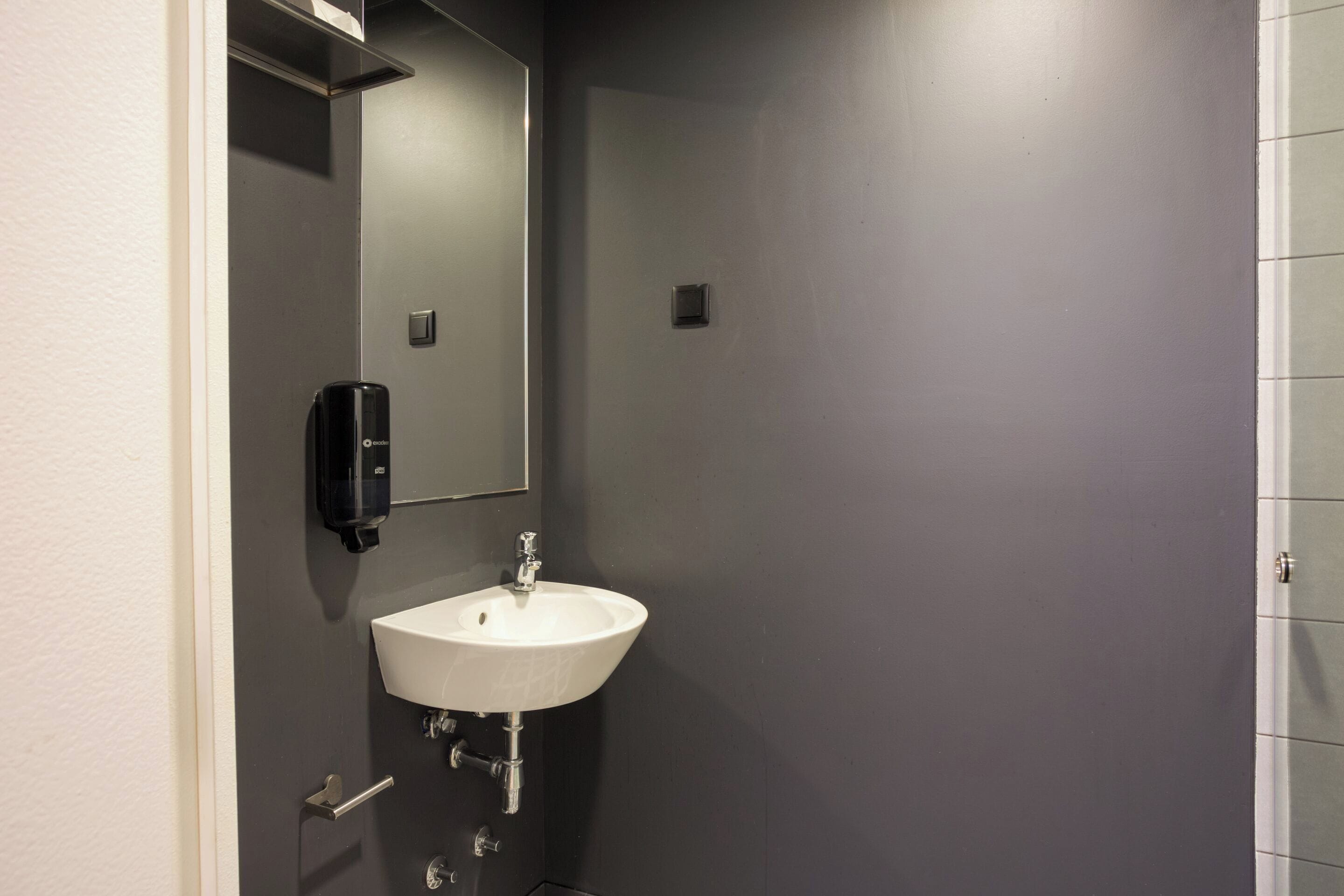 A bathroom with a white sink, a mirror, and a soap dispenser.