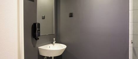 A bathroom with a white sink, a mirror, and a soap dispenser.