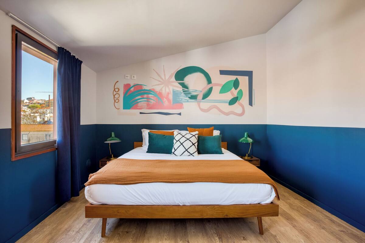 Ein Schlafzimmer mit Bett, Blick auf die Stadt und einer Wandmalerei.