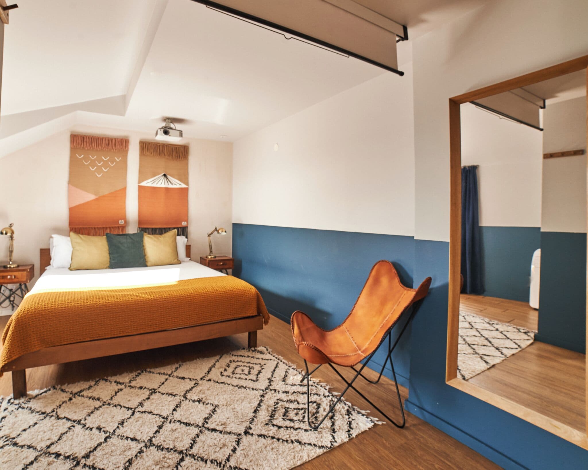 A bedroom with a bed, a chair, a large mirror, and a patterned rug.