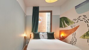 Een bed met houten frame, een raam met gordijnen, wanddecoratie en twee bedlampjes.