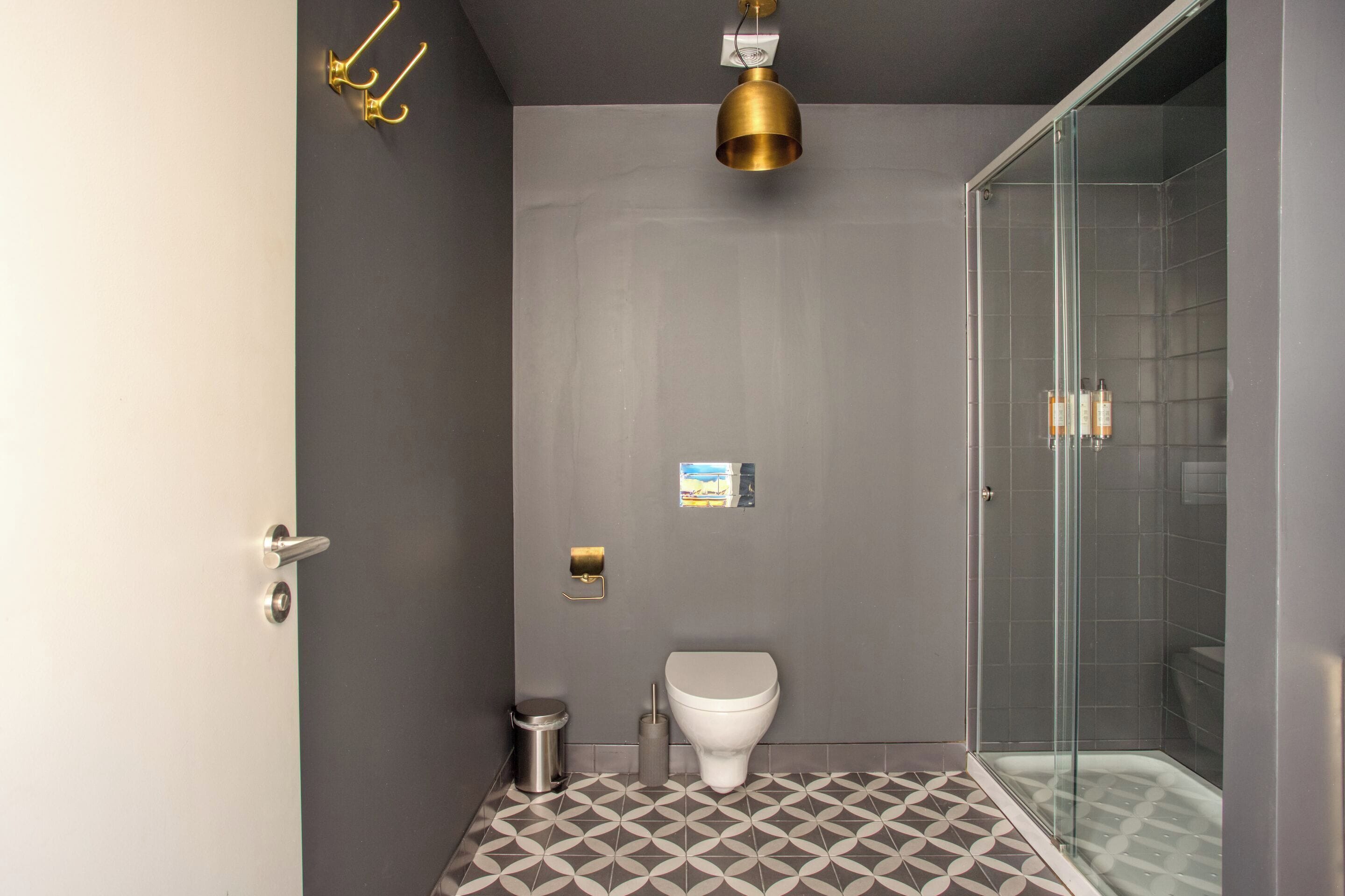 A modern bathroom with a toilet, a trash bin, a shower with a glass door, and a patterned floor.