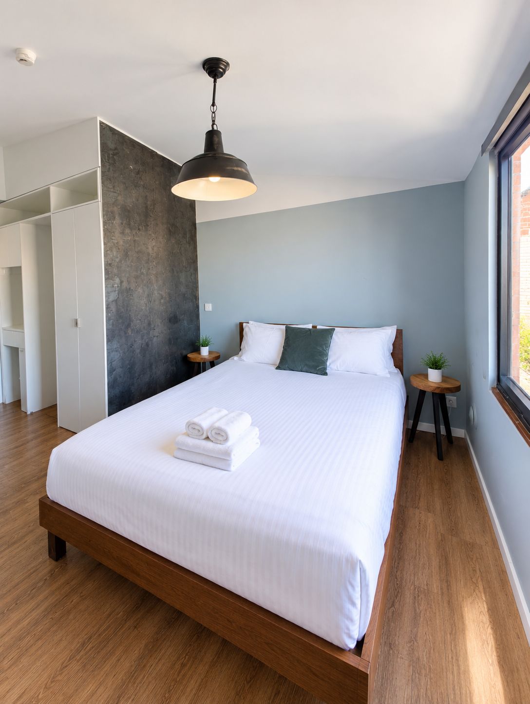 Ein modernes Schlafzimmer mit einem großen Bett, einer Pendelleuchte und einem Blick ins Freie durch ein Fenster.