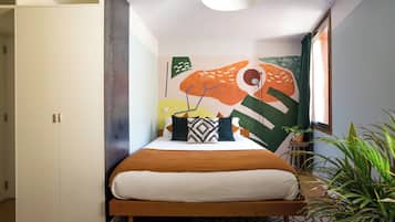 Un dormitorio con cama, armario, pared con arte abstracto, ventana y planta.