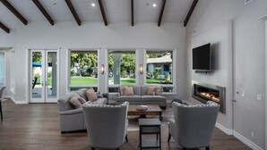 A spacious living room with a fireplace, large windows, and a flat-screen TV.