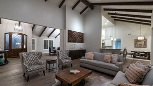 A spacious living room with a high ceiling, wooden beams, and a dining area with a large table and chairs.
