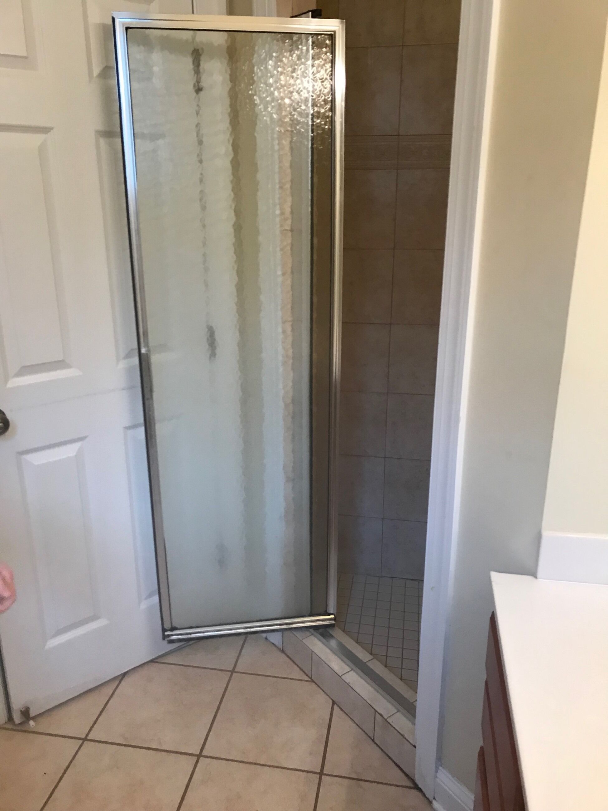 A bathroom with a glass shower enclosure, a white door, and tiled flooring.