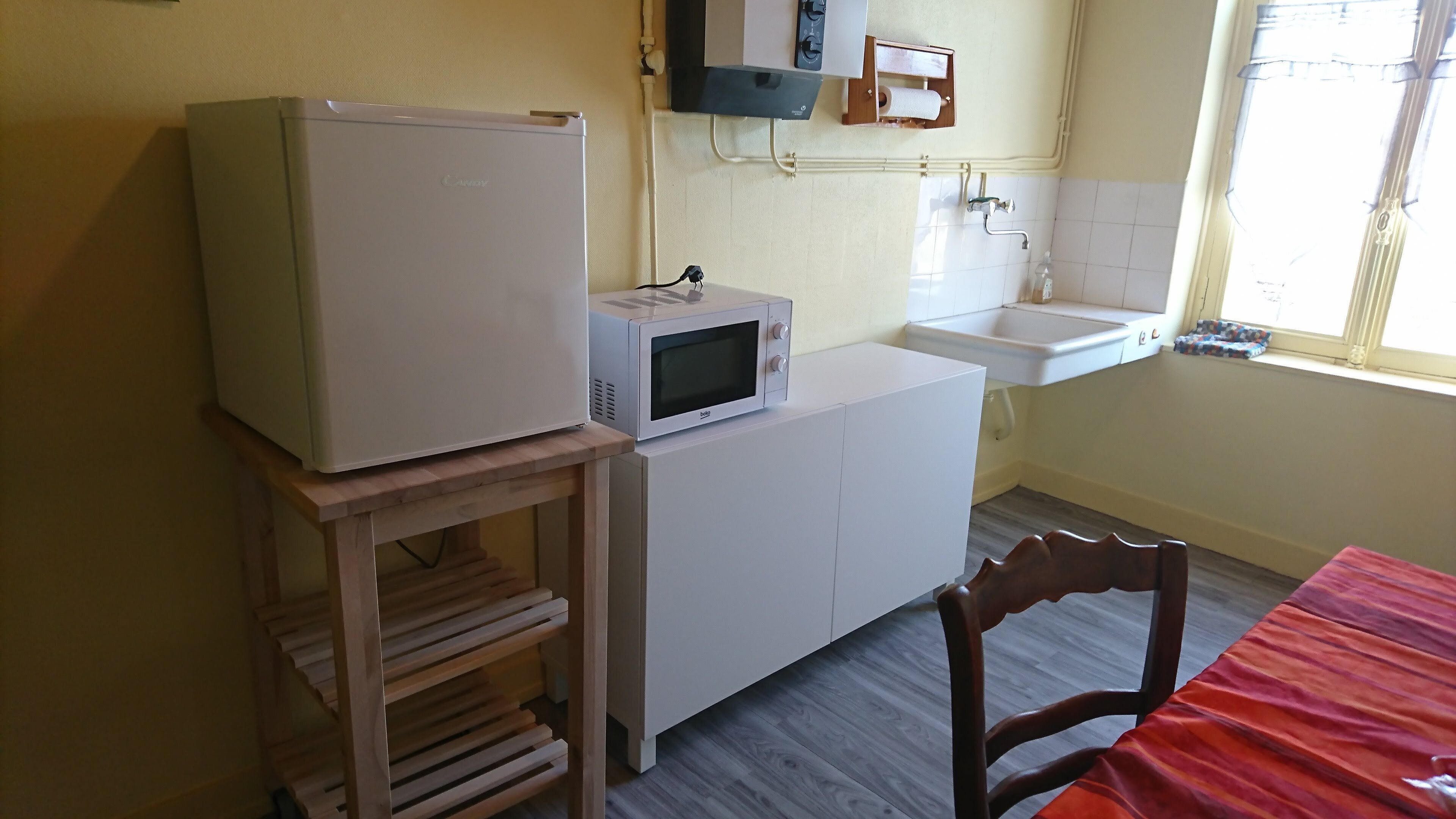 A compact kitchen with a refrigerator, microwave, sink, and wooden chair.