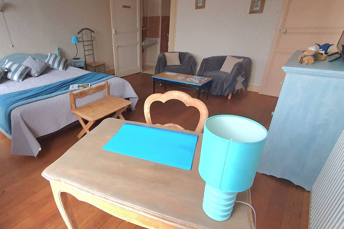 A compact room with a bed, a desk, a chair, a lamp, and a small table.