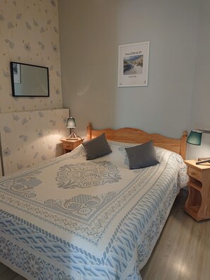 A bedroom with a large bed, two bedside tables, a wall-mounted mirror, and a framed painting.