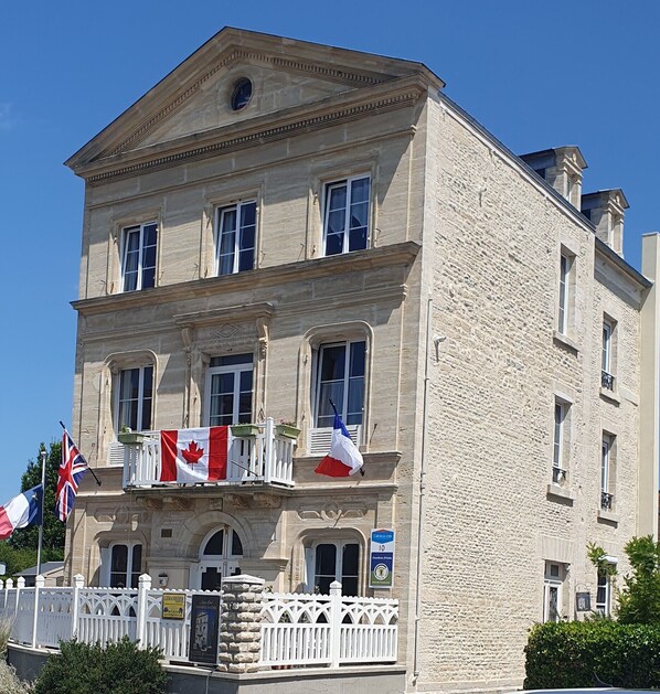 A historic stone building with a symmetrical facade, multiple windows, and a balcony with railings.
