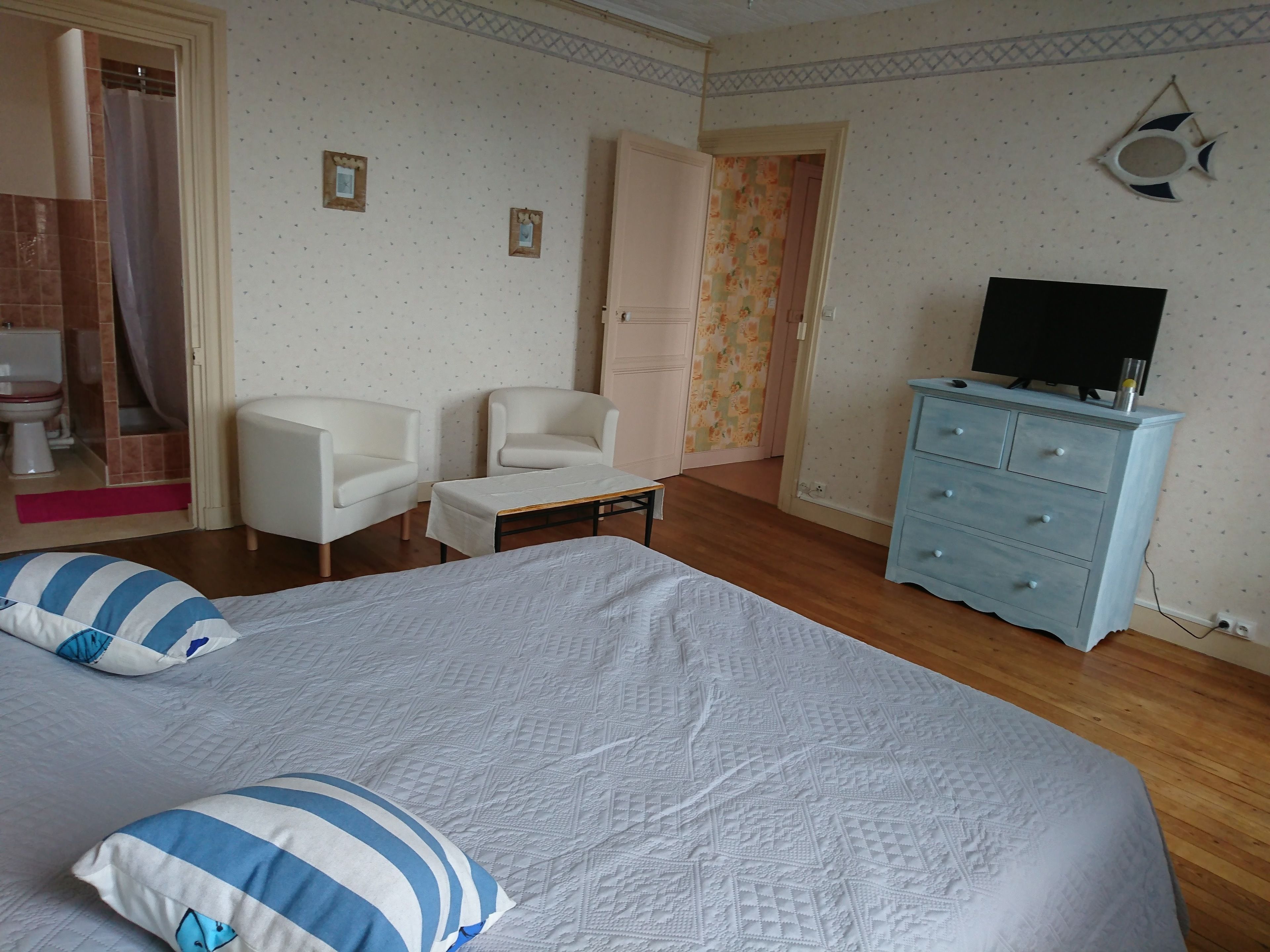 Une chambre à coucher comprenant un lit, deux chaises, une commode et un téléviseur.