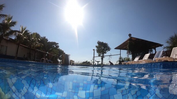 A clear blue pool with tiled patterns, surrounded by palm trees and a shaded area with lounge chairs.