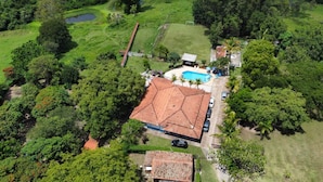 An aerial view of a property with a central building, a swimming pool, and surrounding greenery.