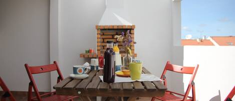 Una mesa de madera con sillas, un horno de ladrillo y diversos utensilios de cocina.
