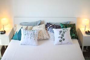 A neatly made bed with a variety of patterned pillows and two bedside lamps.