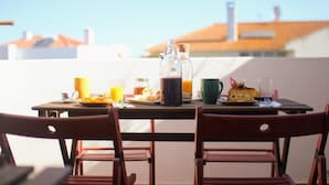 A dining table with breakfast items and drinks, two wooden chairs, and a view of buildings in the background.