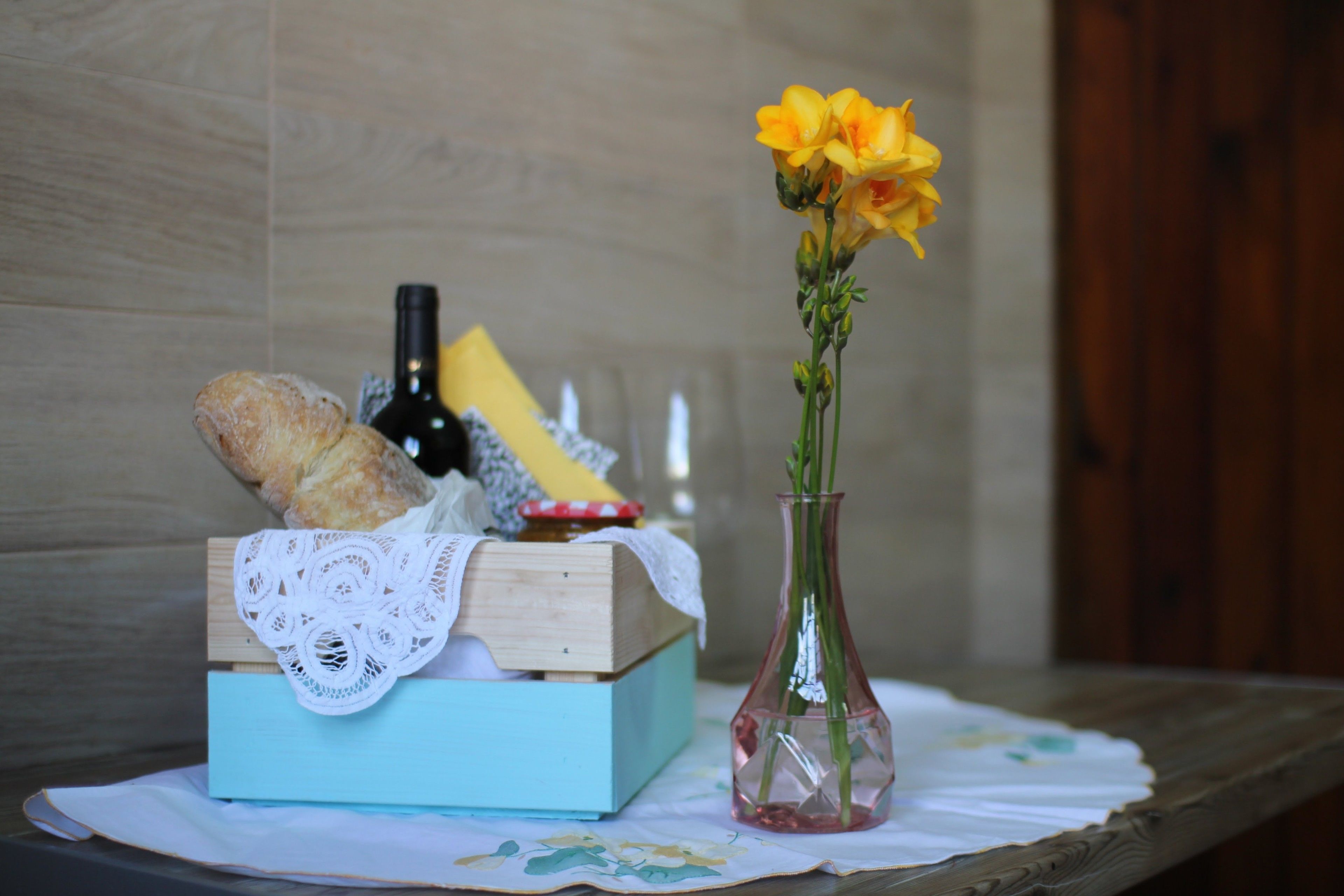A wooden box with a lace cloth, a bottle, and a vase with flowers on a table.