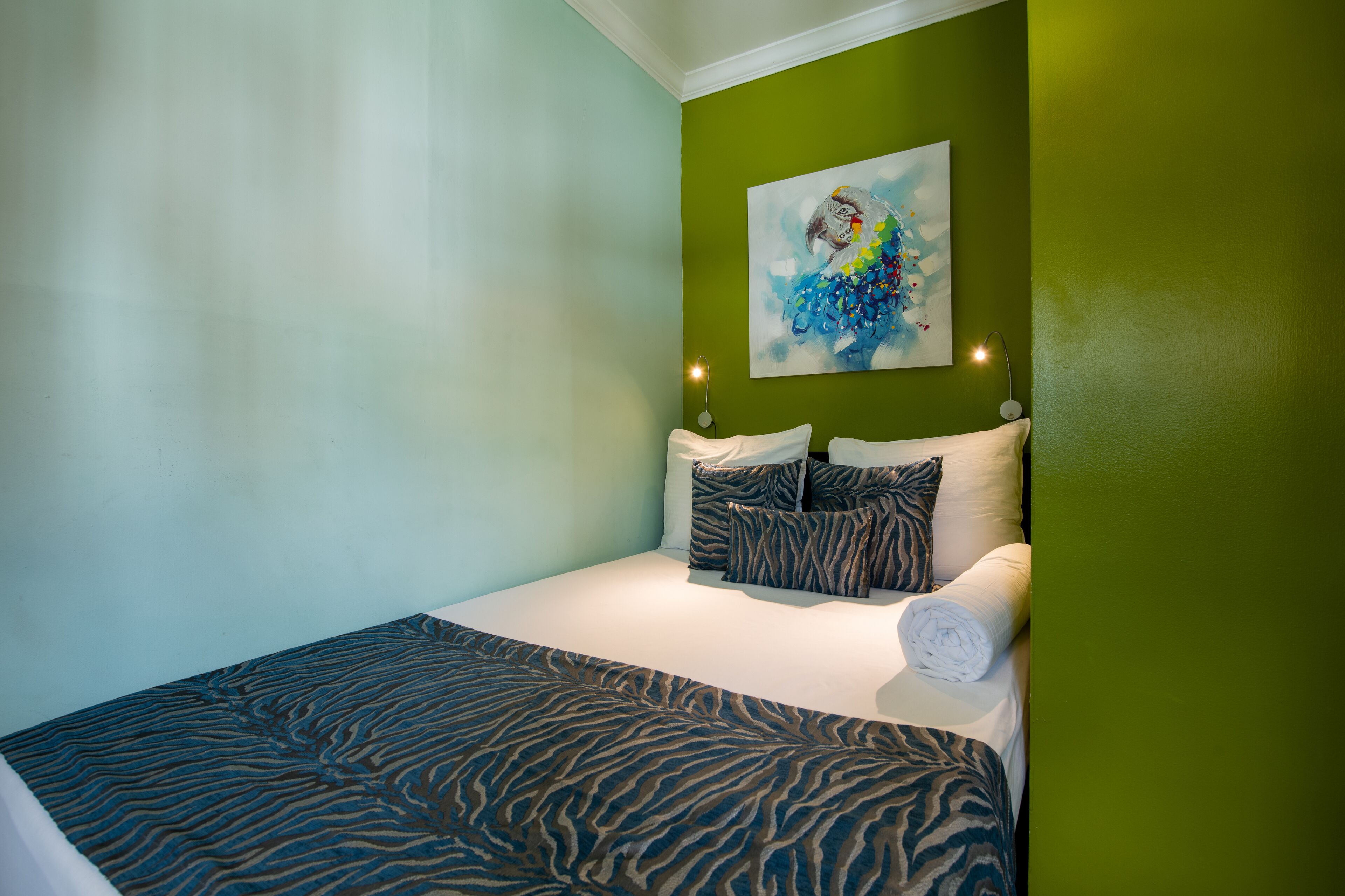 A neatly made bed with a zebra-patterned bedspread, a colorful abstract painting on the wall, and a green accent wall.