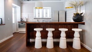 A modern kitchen with a central island, wooden stools, white cabinetry, and a large window. - Villa Amalie (Willemstad)