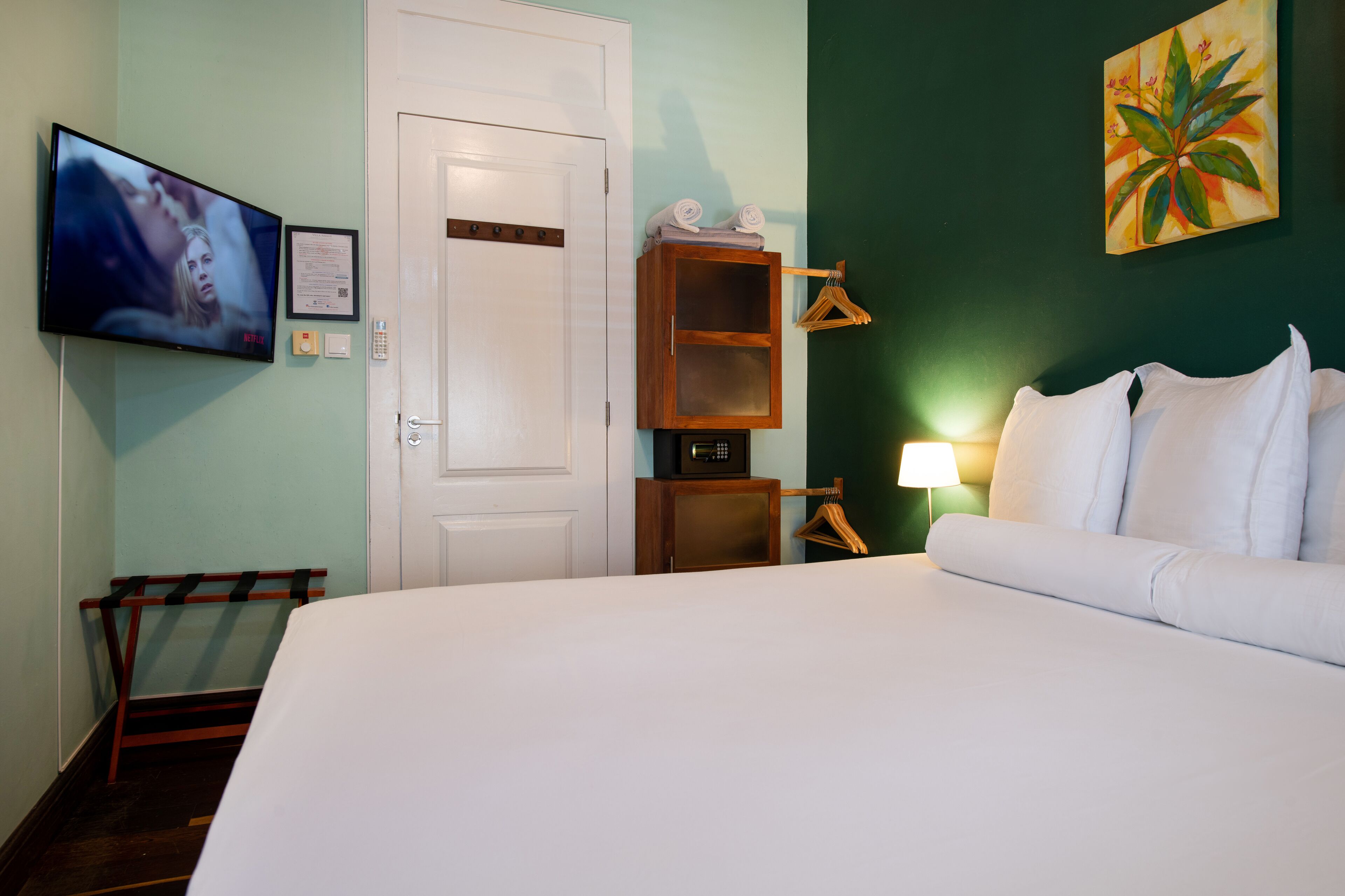 A hotel room with a bed, a television, a wooden cabinet, and a painting on the wall.