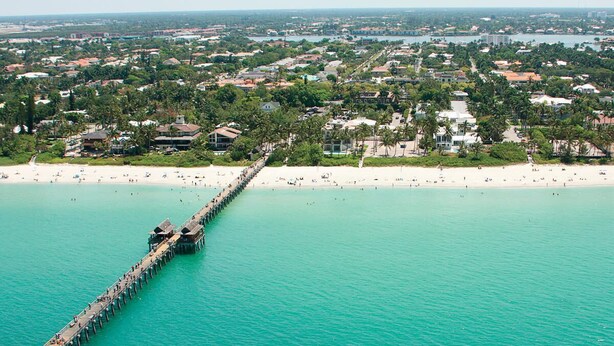 An aerial view of a coastal area with a long pier extending into turquoise waters, surrounded by residential buildings and a sandy beach. - Cozy apart in a quiet neighborhood, with beautiful views. (NAPLES)