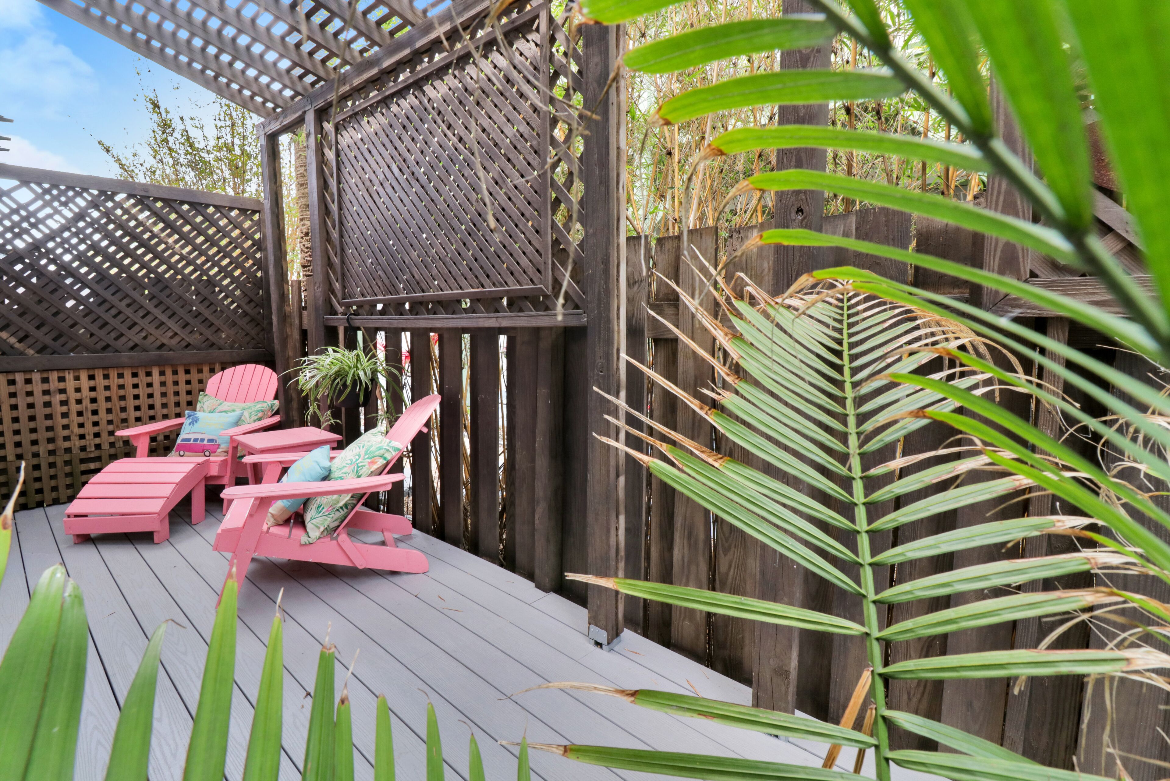 Une terrasse en bois avec des chaises roses et une structure en treillis.