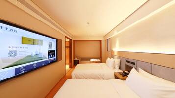 A hotel room with a TV mounted on the wall displaying a room service menu, two beds with white linens, a bedside table with a lamp, and a small round table with a chair.