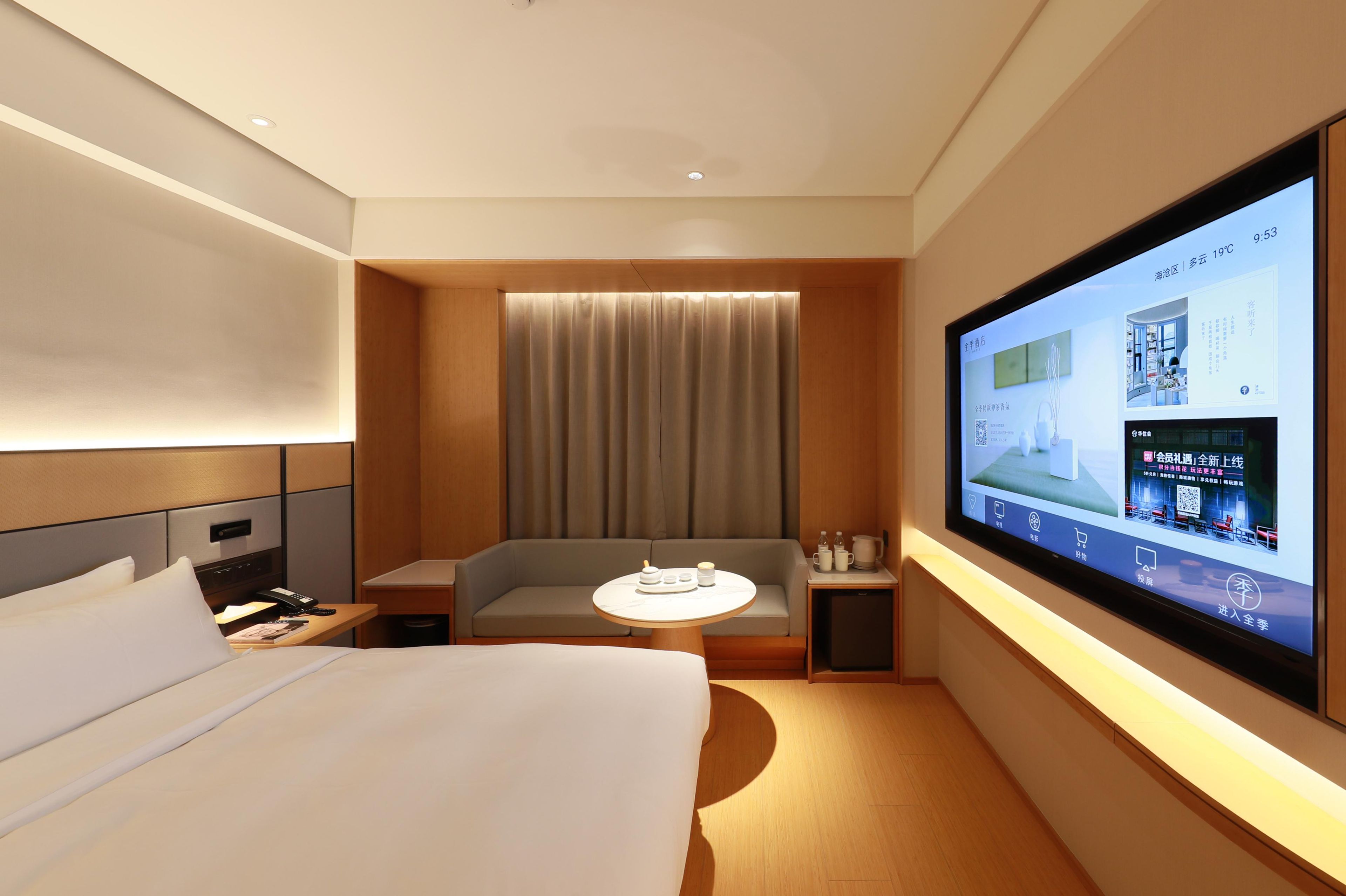 Une chambre d’hôtel moderne, dotée d’un grand lit, d’un canapé, d’une petite table et d’un téléviseur affichant des informations sur la chambre.