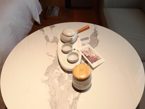 Une table ronde en marbre, sur laquelle se trouvent un service à thé, un récipient en bois et une carte.