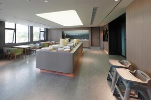 Ein moderner Essbereich mit einer zentralen Buffetstation, Sitzgelegenheiten und großen Fenstern, die für natürliches Licht sorgen.