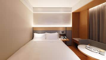 Une chambre d’hôtel moderne avec un lit bien fait, une table de chevet avec une lampe et un petit coin salon avec une table.