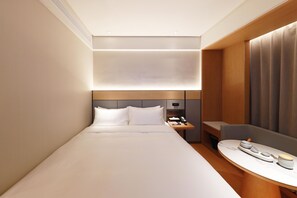 A modern hotel room with a neatly made bed, a bedside table with a lamp, and a small seating area with a table.