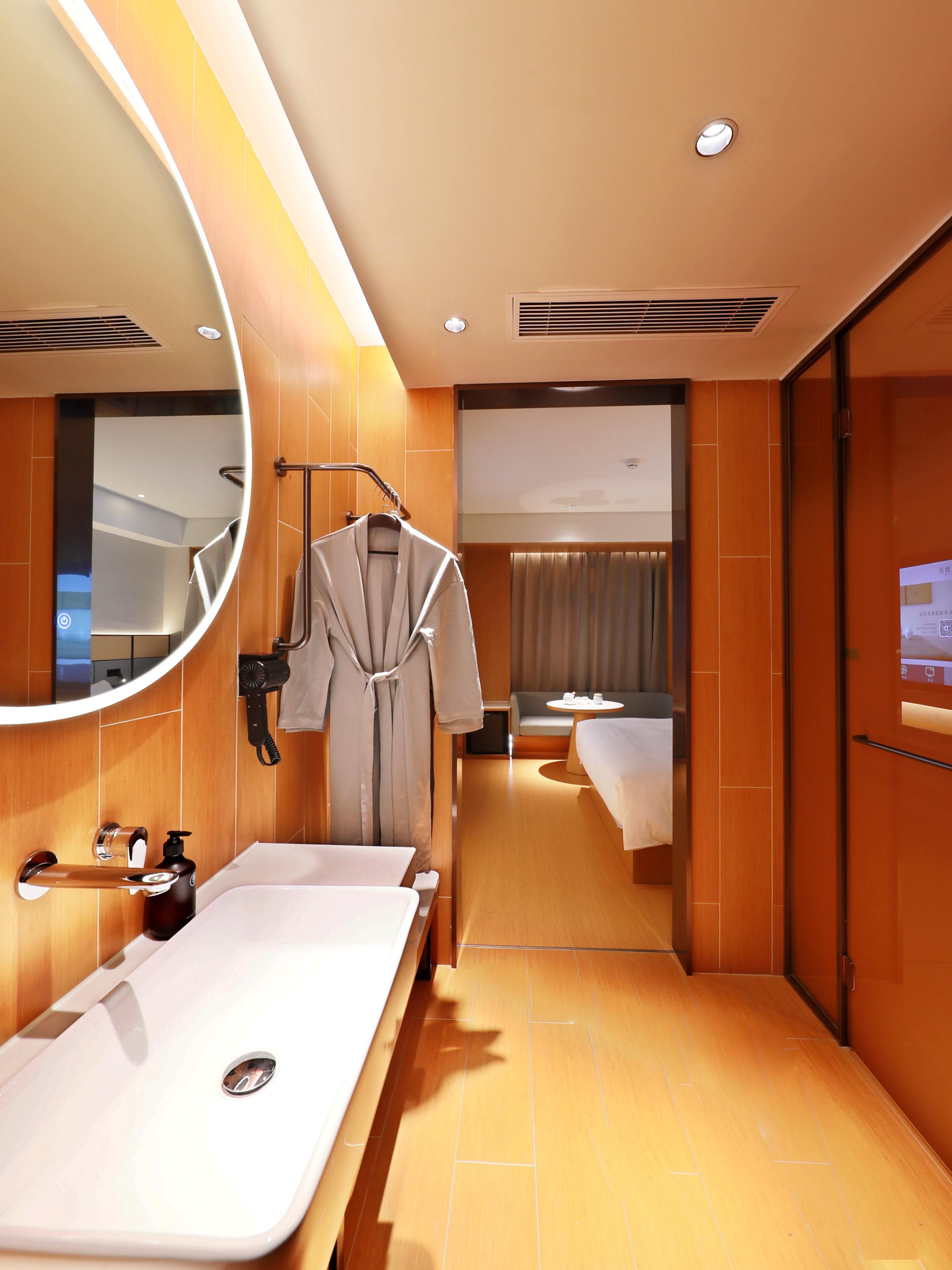 A hotel bathroom with a large mirror, a sink, a robe hanging, and a shower area.