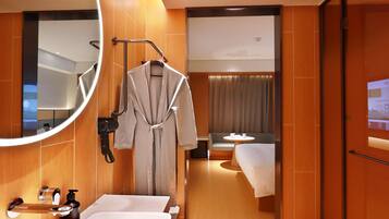 A hotel bathroom with a large mirror, a sink, a robe hanging, and a shower area.