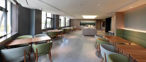 Un espace de restauration moderne doté de plusieurs tables et chaises, de grandes fenêtres et d’un îlot central avec un comptoir.