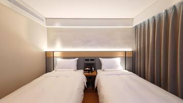 A hotel room with two single beds, a bedside table with a lamp, and a large window with curtains.