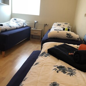 A bedroom with two single beds, a nightstand with a lamp, and a window providing natural light.