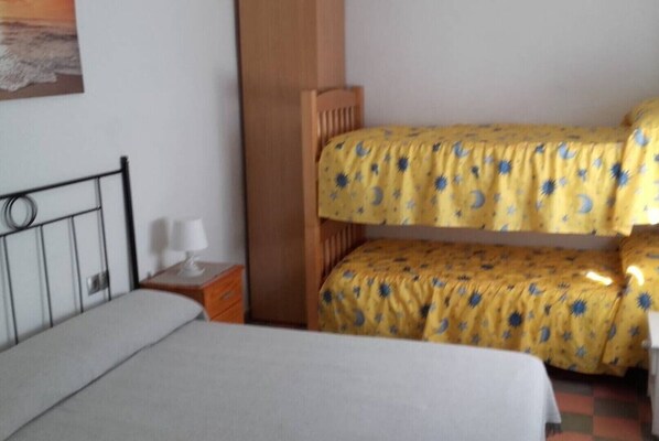 A room with a bunk bed, a single bed, a nightstand with a lamp, and a wall-mounted painting.