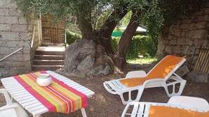 Een terras met een tafel en twee loungestoelen, een grote rots en een houten poort op de achtergrond.