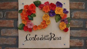 Un letrero de madera con un arreglo de rosas de colores en forma de corazón y el texto 'Corte delle Rose'.