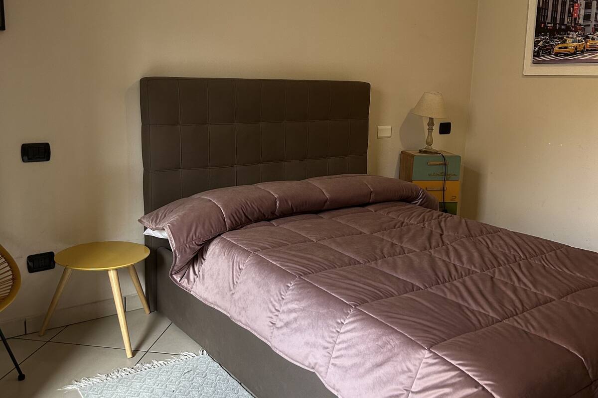 A bedroom with a bed, a small round table, a lamp, and a framed picture on the wall.